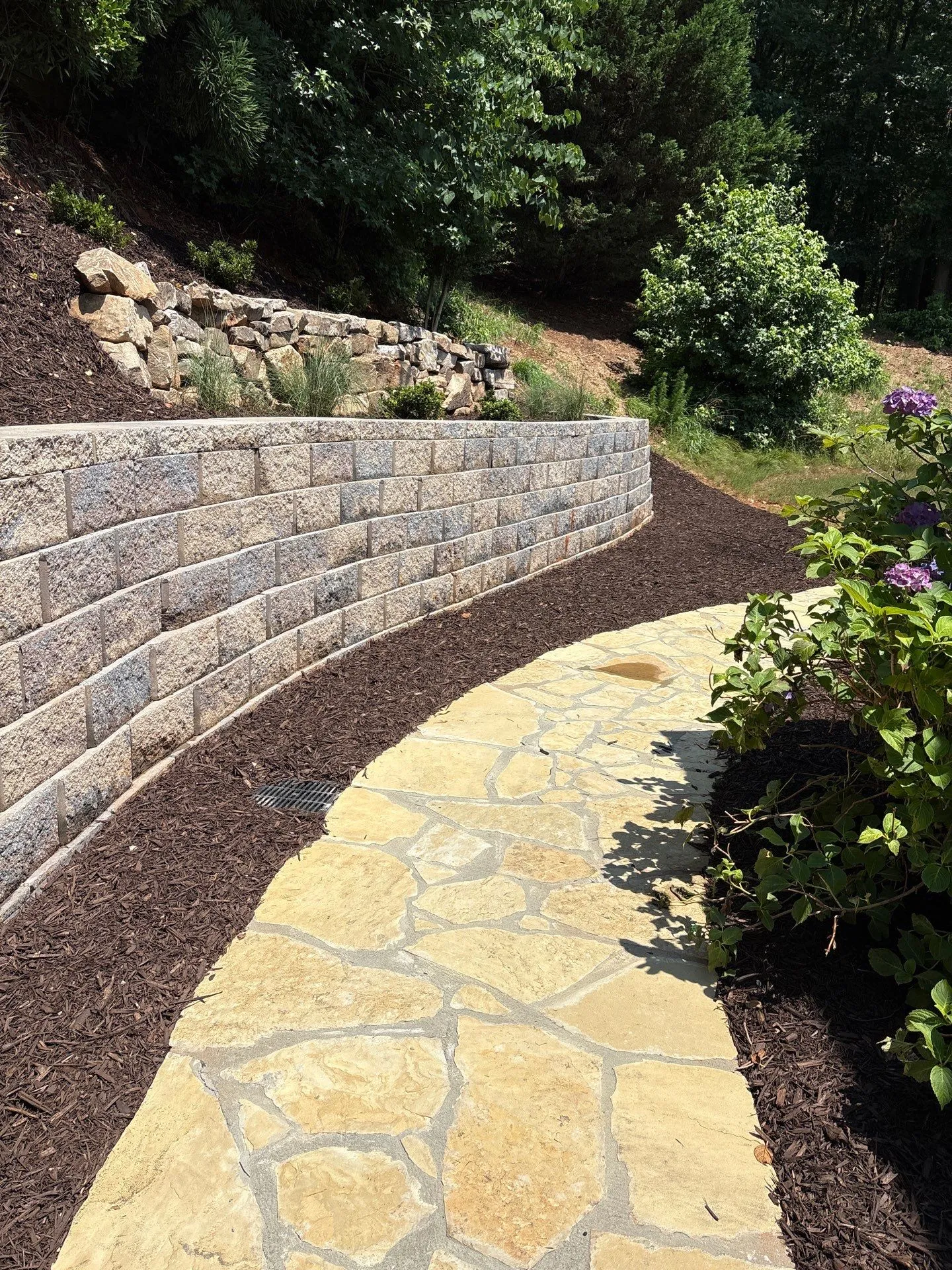 Curved stone retaining wall along a mulched garden bed with a flagstone path beside it.